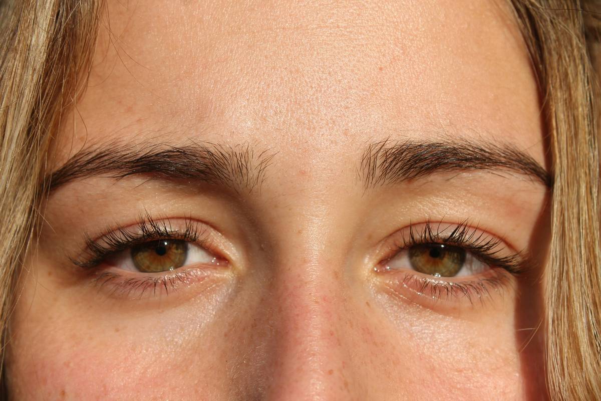 Professional using a precise brow trimming tool on model's eyebrow