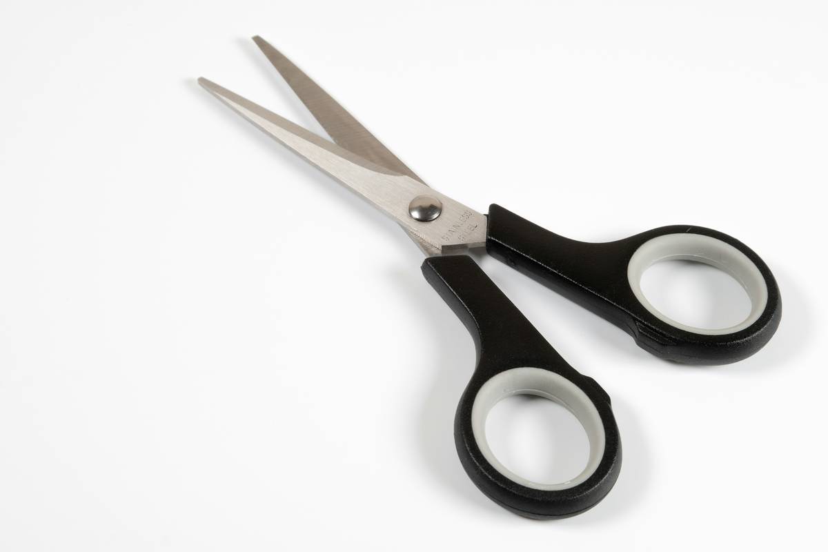 Close-up of high-precision brow scissors trimming a single eyebrow hair at 45-degree angle